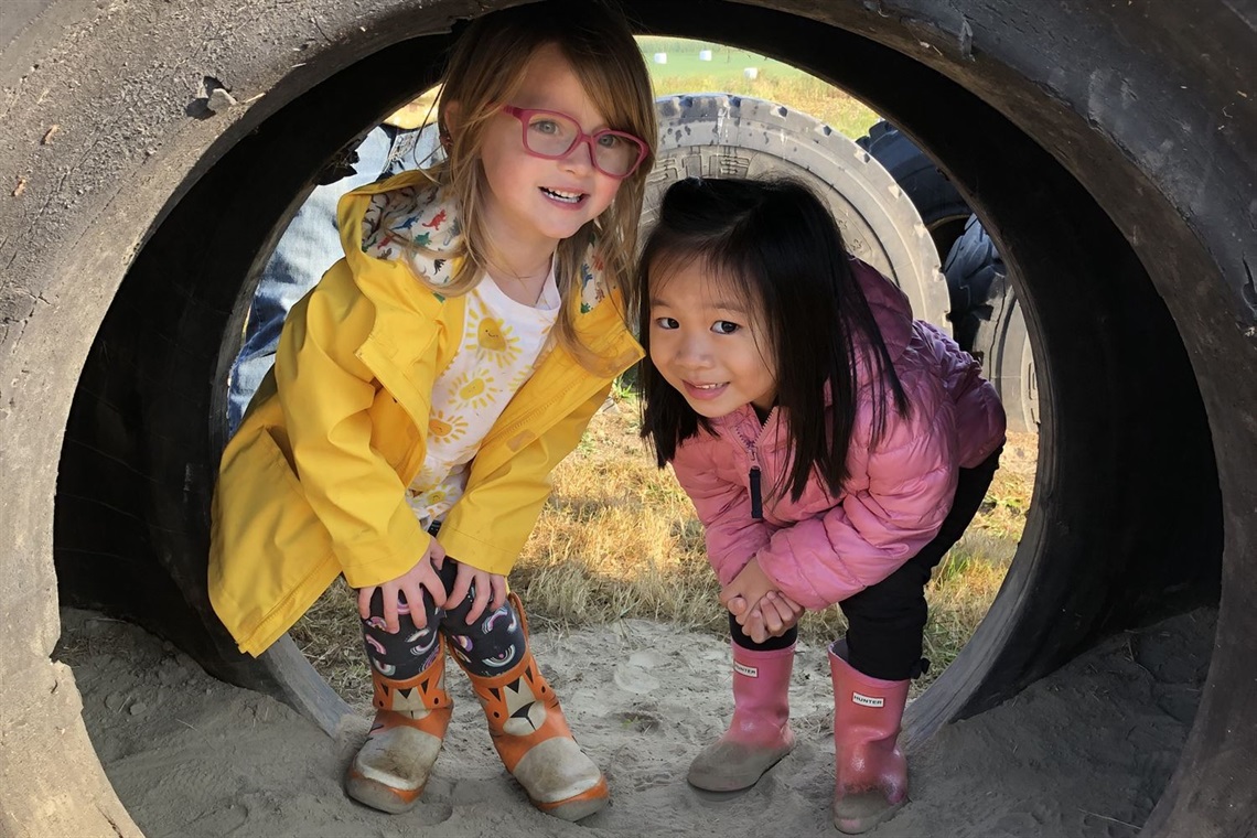 two girls hiding in a old tractor tire